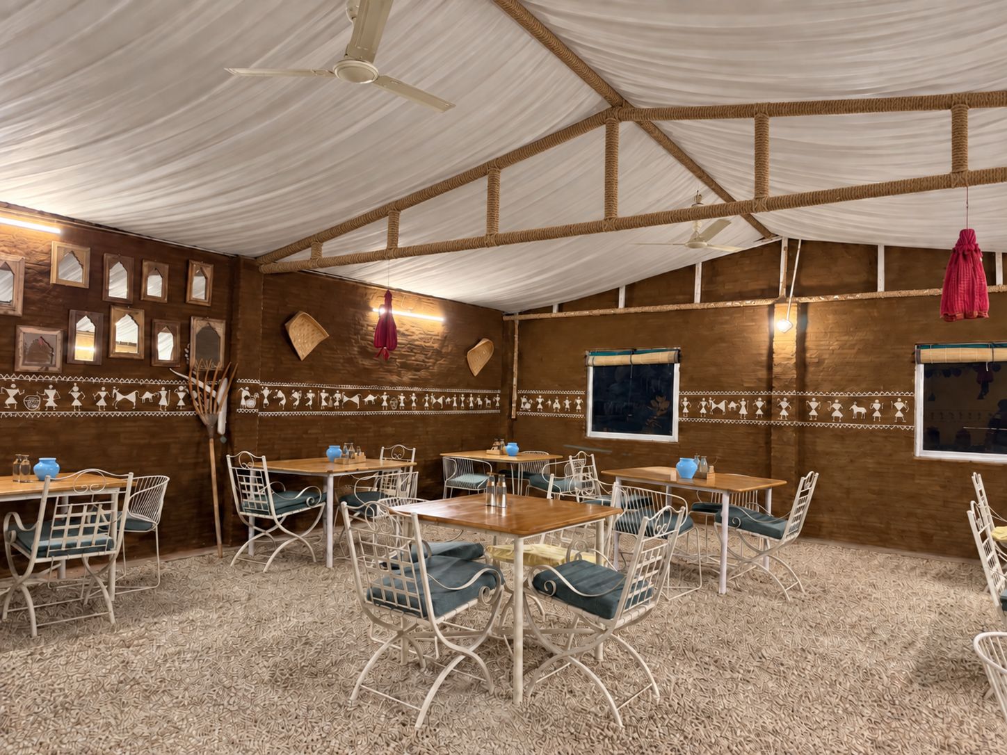 A room with a high ceiling, white ceiling fans, wooden walls, and a patterned carpet. Tables and chairs are arranged for dining.