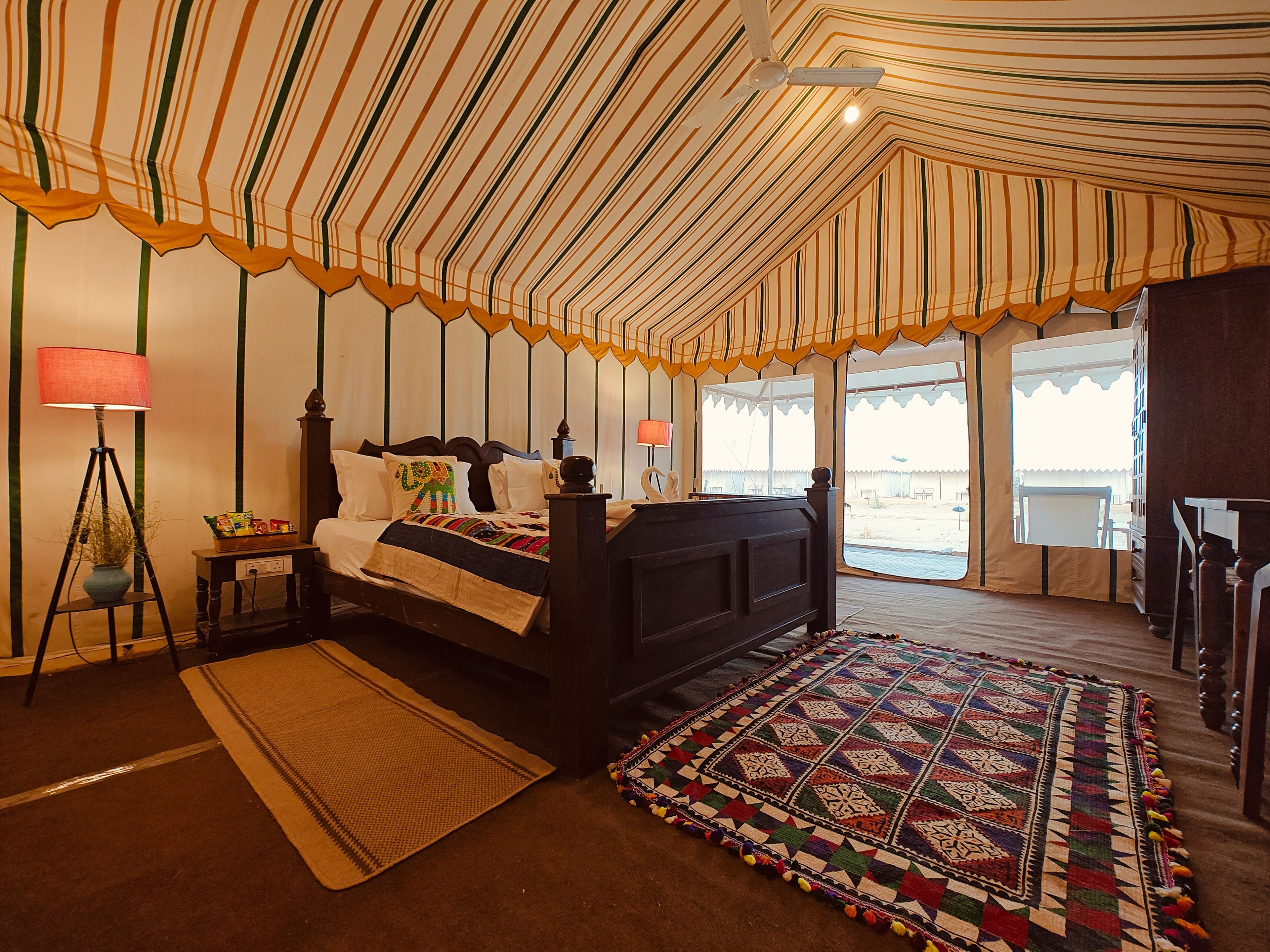 A tent-style room with a bed, a lamp, a rug, and a view of the outside.