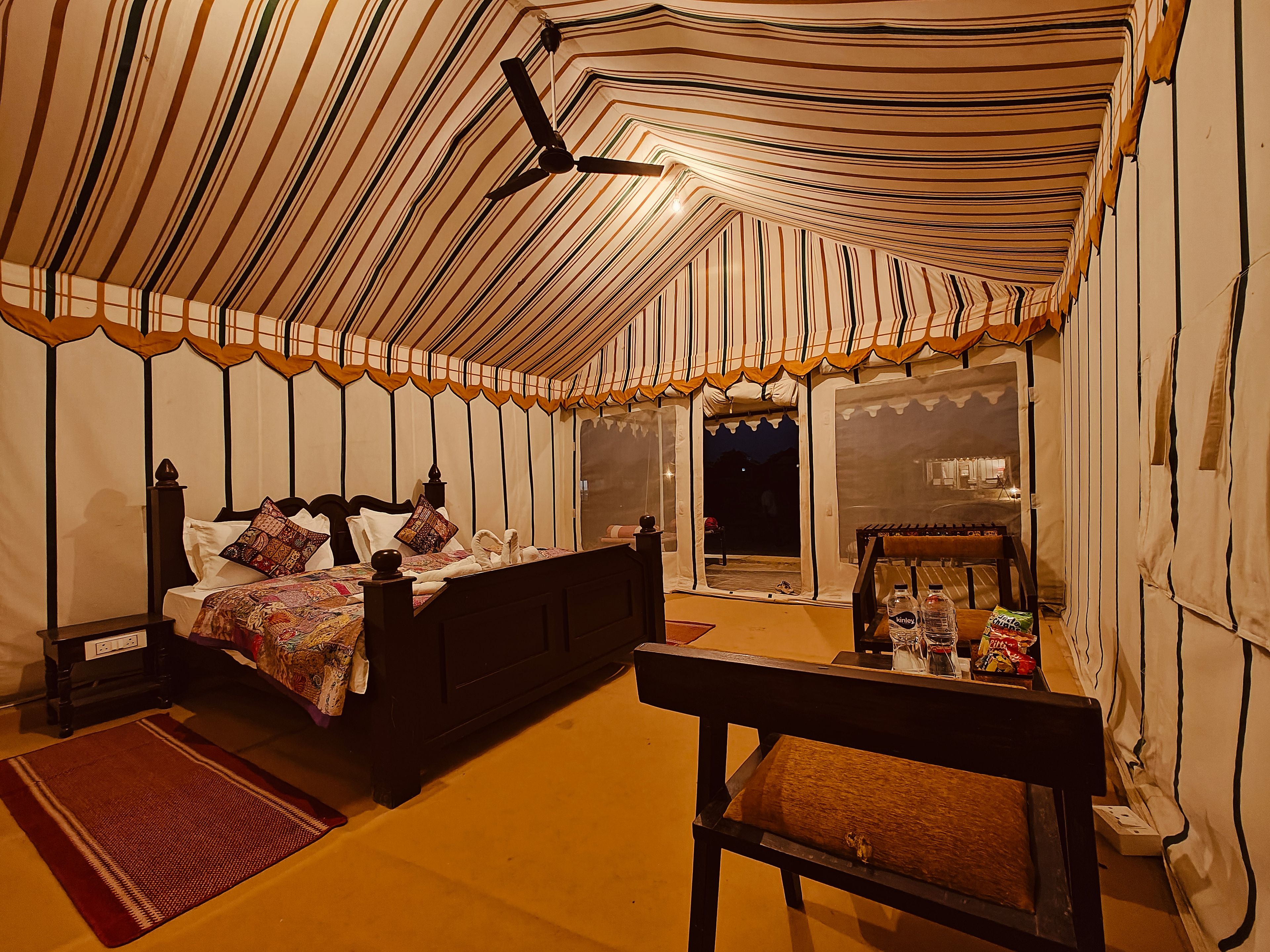 Una habitación con carpa, una cama, un banco y una mesa con objetos encima.