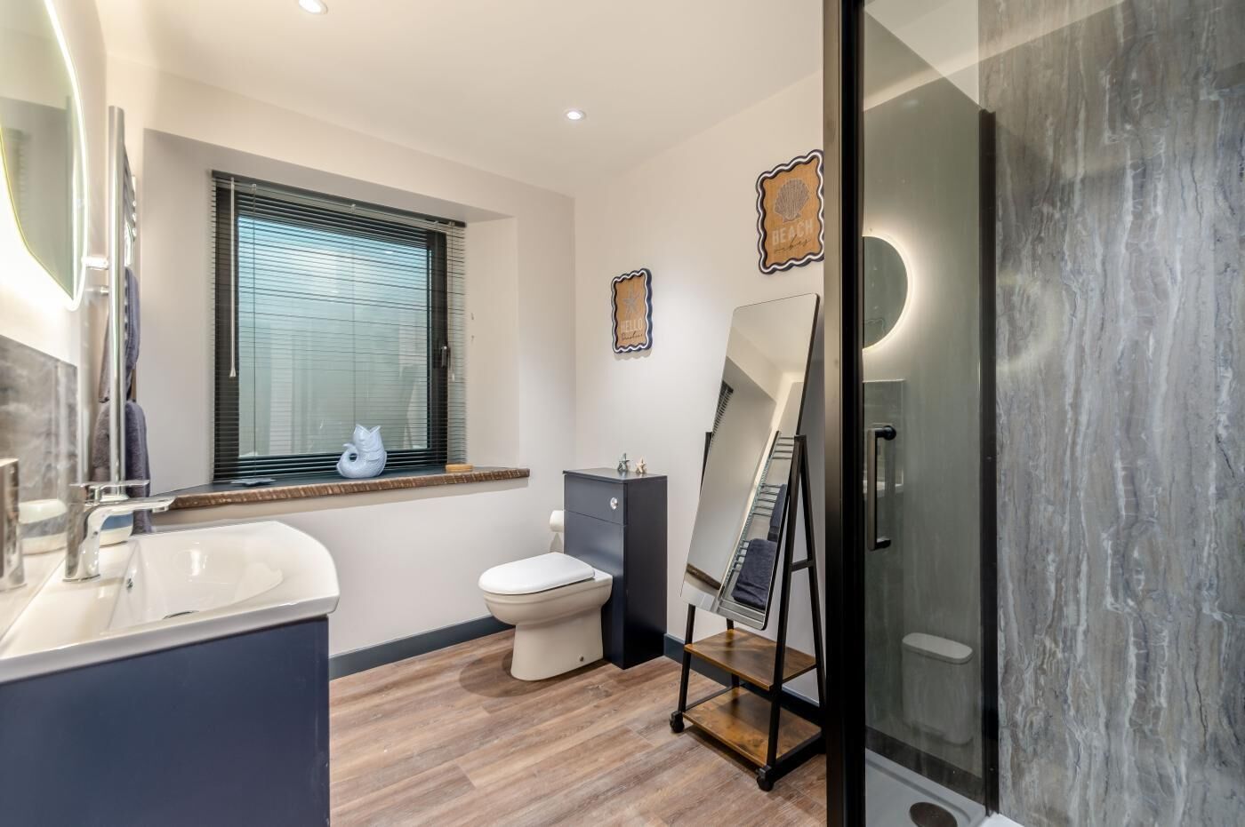 Un baño moderno con un espejo grande, un inodoro, un mueble de tocador y una ventana con persianas.