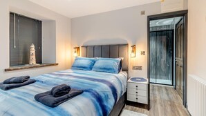 Ein Schlafzimmer mit Bett, Nachttisch, Lampe und Blick auf eine Glastür, die zu einem Balkon führt.