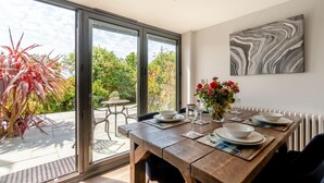 Ein Essbereich mit Tisch für zwei Personen, einer Blumenvase und Blick auf den Garten durch große Schiebetüren.