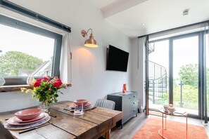 A modern dining area with a wooden table, pink plates, and a vase of flowers. - 1 Bed in Tenby (oc-b41401) (Tenby)