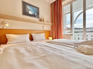 A hotel room with two beds, a painting, a window with curtains, and a view of the sea. - Ferienwohnung im Seepark Sellin mit Balkon (Sellin)