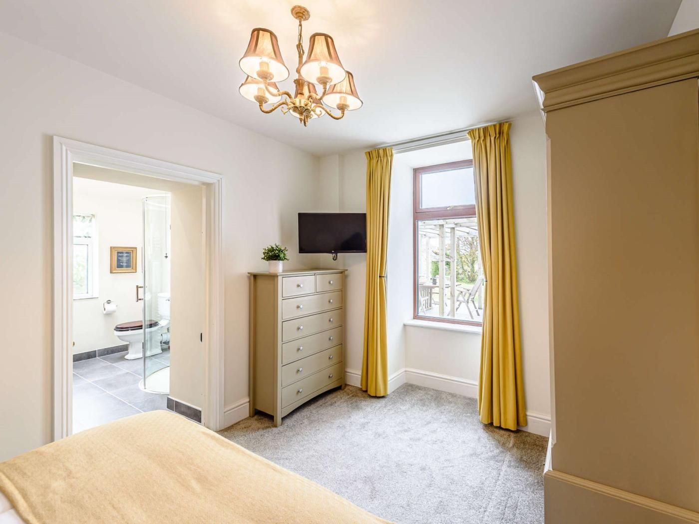 A bedroom with a bed, a dresser, a TV, and a window with curtains.