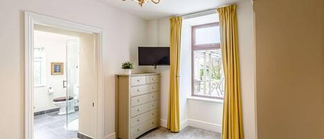 A bedroom with a bed, a dresser, a TV, and a window with curtains.