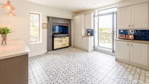 A modern kitchen with a built-in stove, white cabinets, and patterned floor tiles. - 7 Bed in Holyhead (oc-55866) (Bae Trearddur)