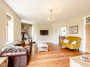 A living room with a fireplace, leather sofa, yellow armchair, and a television. - 7 Bed in Holyhead (oc-55866) (Bae Trearddur)