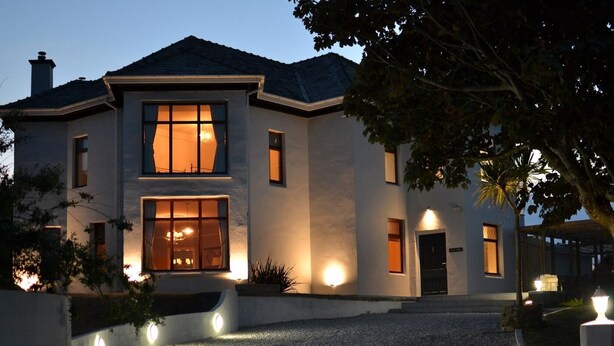 A modern two-story house with a well-lit entrance, a covered patio, and a gravel driveway. - 7 Bed in Holyhead (oc-55866) (Bae Trearddur)