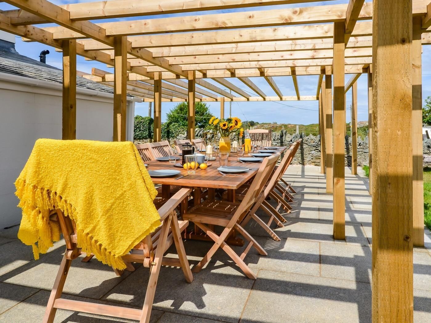 An outdoor wooden pergola with a dining table set for six, surrounded by chairs.