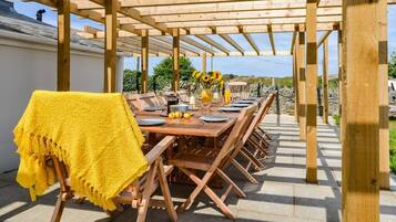An outdoor wooden pergola with a dining table set for six, surrounded by chairs.