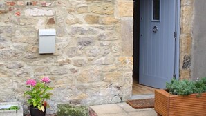 A stone wall, a grey door, a mailbox, and a planter with flowers. - 2 Bed in Warkworth (oc-coq139) (Warkworth)