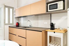 Cocina compacta con microondas, cafetera y un mueble pequeño.