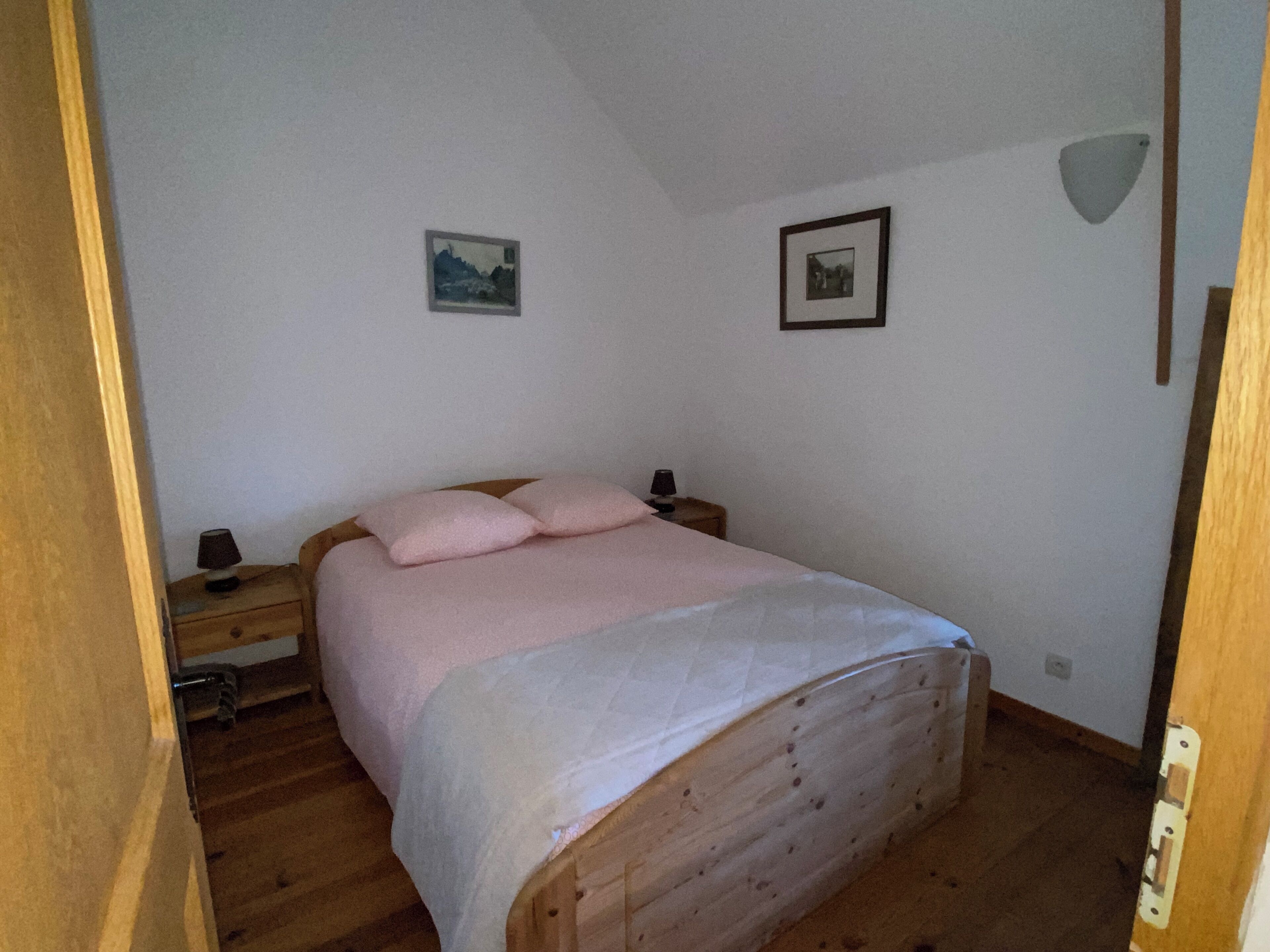 A bedroom with a wooden bed, a nightstand, a lamp, and two framed pictures on the wall.