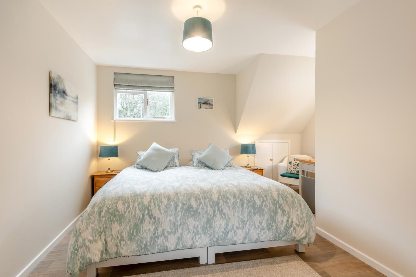 Une chambre à coucher comprenant un lit, deux lampes de chevet, une fenêtre, une porte et un petit bureau avec une chaise.