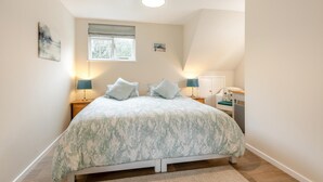 A bedroom with a bed, two bedside lamps, a window, a door, and a small desk with a chair.