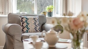 A cozy room with a grey sofa, a patterned cushion, a table with a teapot, cups, and a vase with flowers.