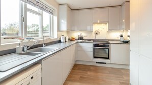 A modern kitchen with white cabinets, a built-in oven, a dishwasher, and a window with a view of trees.