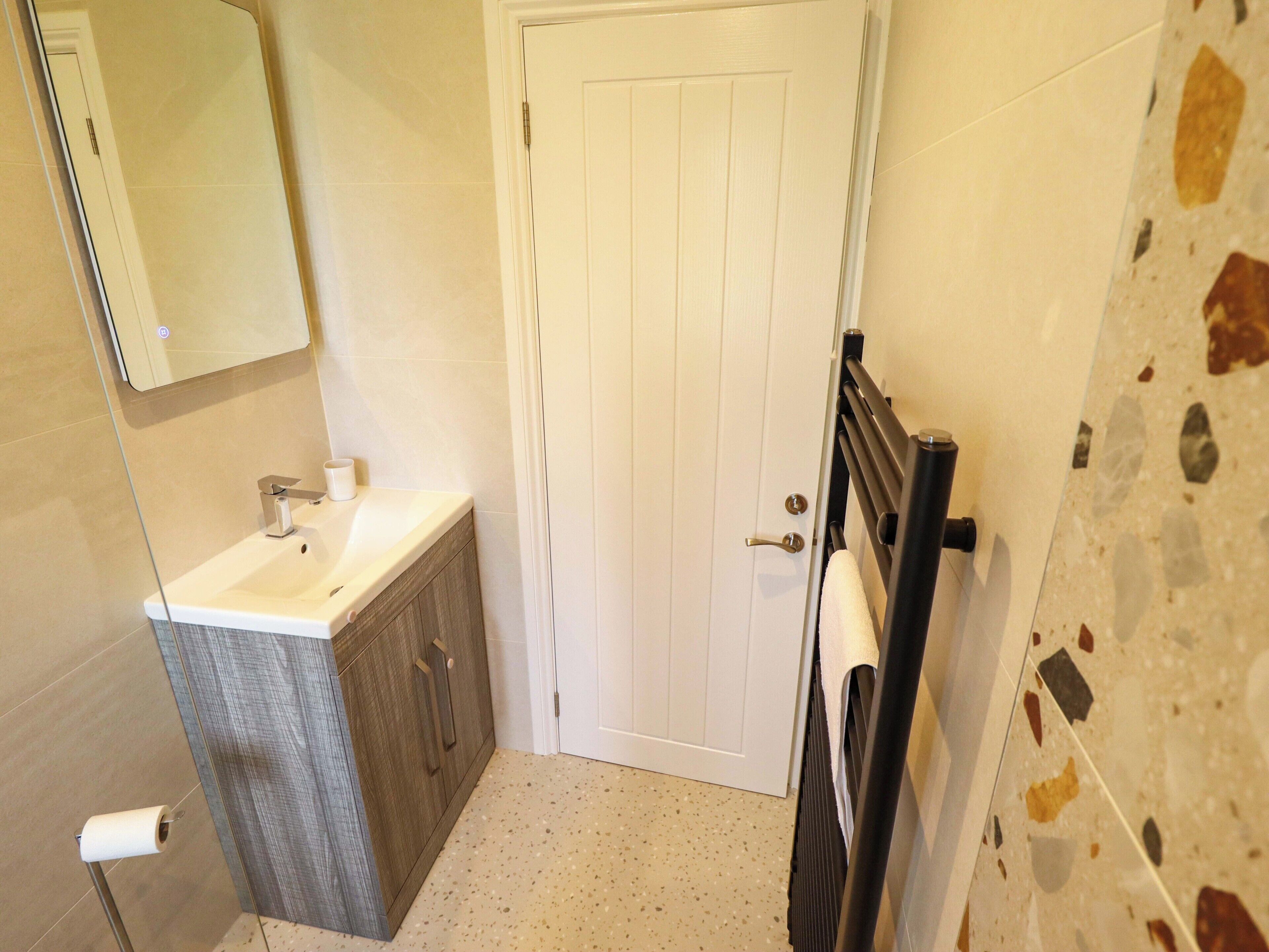 Une salle de bain avec une porte blanche, un lavabo surmonté d’un miroir et un porte-serviettes fixé au mur.