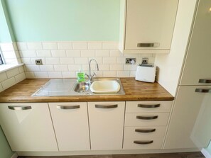Una cocina con un lavamanos de acero inoxidable, un tostador y una botella de jabón para manos.