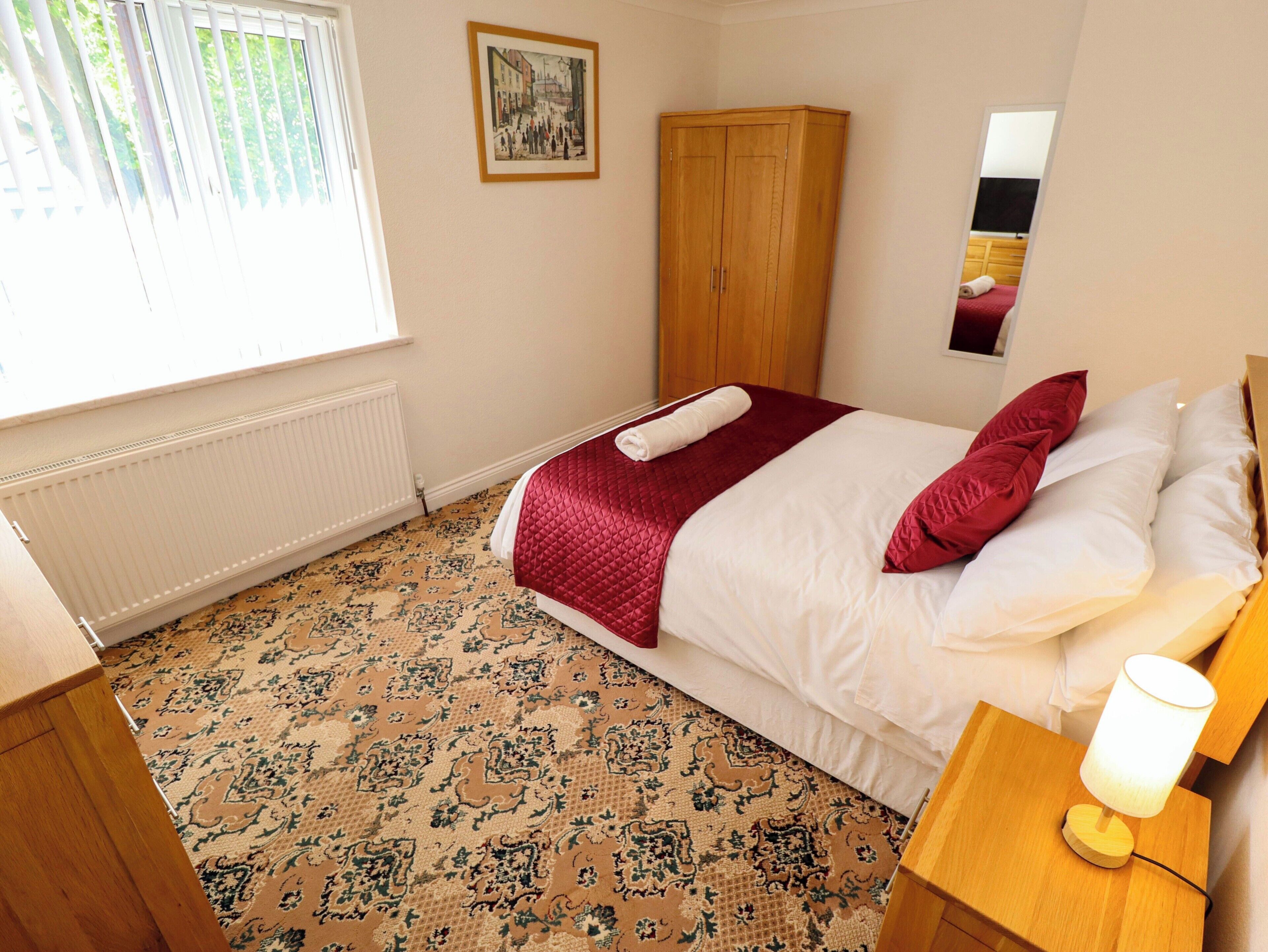 Un dormitorio con cama, un armario de madera, radiador, alfombra estampada y un cuadro en la pared.