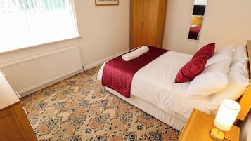 Un dormitorio con cama, un armario de madera, radiador, alfombra estampada y un cuadro en la pared.