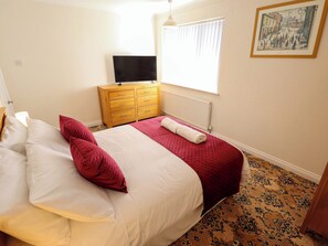 A bedroom with a bed, a dresser, a television, a window with blinds, and a patterned carpet. - 271 Wragby Road (Lincoln)