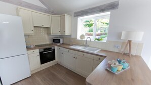 Cucina con mobili bianchi, forno a microonde, lavello e finestra vista giardino.