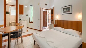 Hotellihuone, jossa on sänky, työpöytä, tuoli, pieni keittiö ja kylpyhuone.
