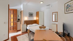Hotellihuone, jossa on sänky, yöpöytä, tuoli, työpöytä ja televisio.