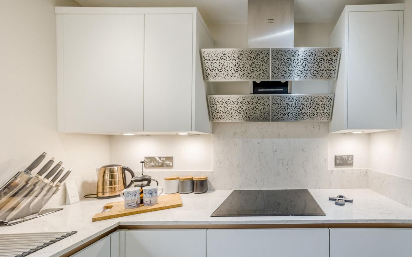 Eine moderne Küche mit weißen Schränken, einem schwarzen Induktionskochfeld und einer gestreiften Spritzschutzwand.