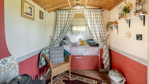 Una habitación acogedora con una cama, una silla de mimbre, una mesita y una estantería con adornos.