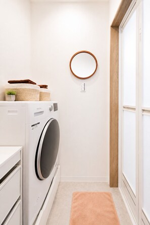 A compact laundry room with a washing machine, a drying rack, and a mirror on the wall. - New Construction | Right Next to Asakusa and the Skytree! | Sleeps 5 | 6-minute walk from the station | 26 ㎡ | High-speed Wi-Fi | 3 beds | (墨田区)