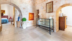 Una habitación con paredes de piedra, un vitrina de vidrio, un aparador de madera y una cama con colcha azul.