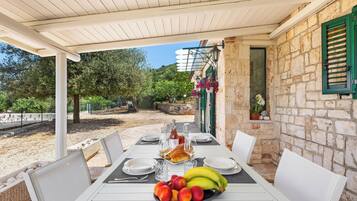 A covered outdoor dining area with stone walls, a table set with plates, glasses, and a fruit bowl.