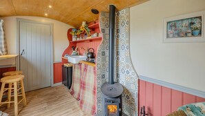 A cozy kitchen with a wood-burning stove, a sink, and a wooden stool. - 1 Bed in Edgefield (oc-c39014) (Edgefield)