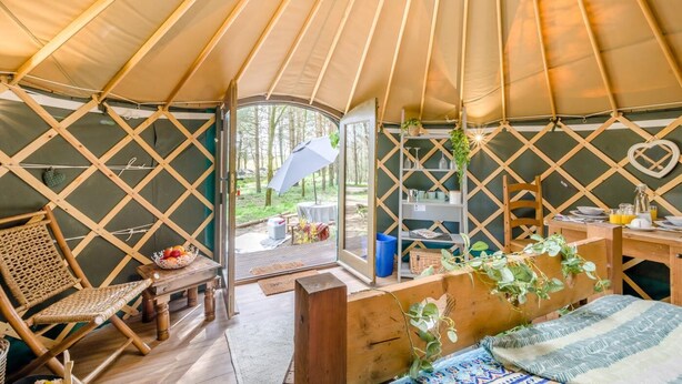 Un interior acogedor de una yurta, con revestimiento de madera, una zona de comedor y vistas al bosque.