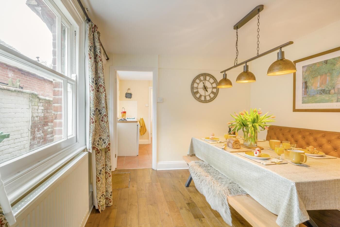 A dining area with a table set for breakfast, a clock on the wall, and a window with curtains.