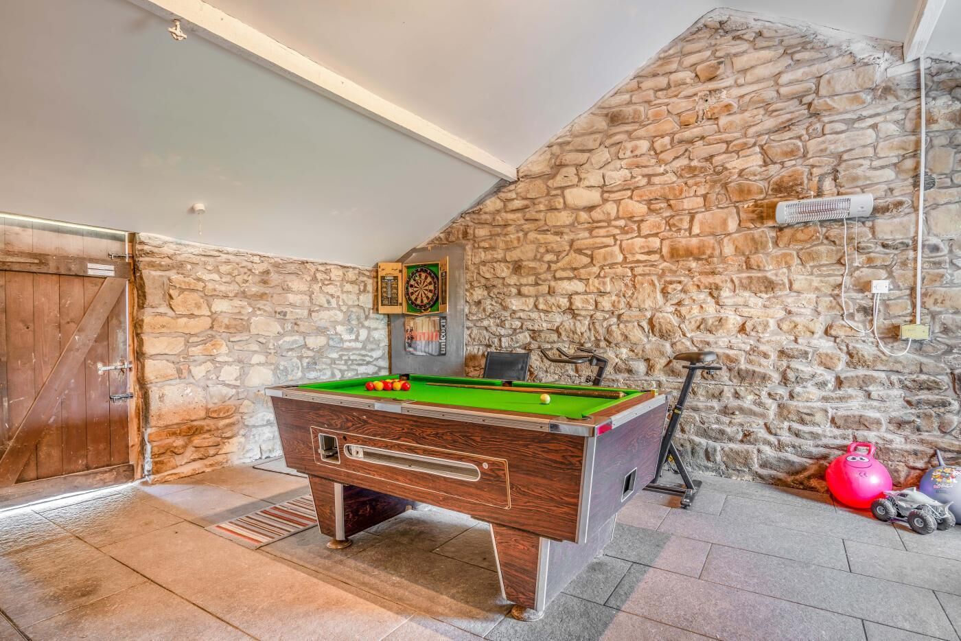 Una mesa de billar en una habitación con paredes de piedra y una puerta de madera.