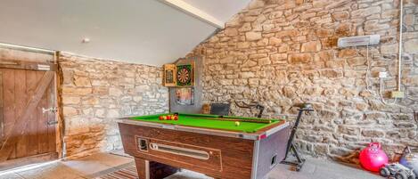 Una mesa de billar en una habitación con paredes de piedra y una puerta de madera.