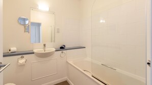 A bathroom with a sink, mirror, toilet, and a shower area.