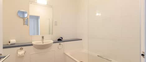 Un baño con lavamanos, espejo, inodoro y zona de ducha.