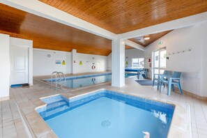 An indoor swimming pool with tiled flooring, wooden ceiling beams, and a seating area with chairs. - 2 Bed in Putsborough (oc-s40237) (Croyde)