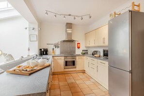 A modern kitchen with a built-in oven, a stainless steel refrigerator, and a dining area with a tray of food. - 2 Bed in Putsborough (oc-s40237) (Croyde)