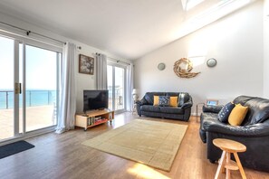 A living room with a TV, two sofas, a rug, and a balcony with a view. - 2 Bed in Putsborough (oc-s40237) (Croyde)