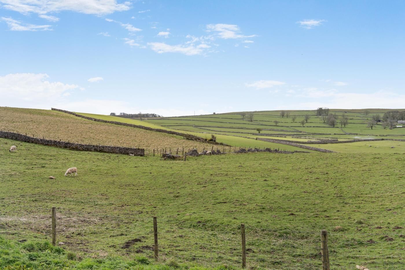A rural landscape with rolling hills, a stone wall, and a fenced field.