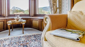 Una habitación con ventanal panorámico, una mesita con jarrón y taza, alfombra estampada y sofá con una revista.