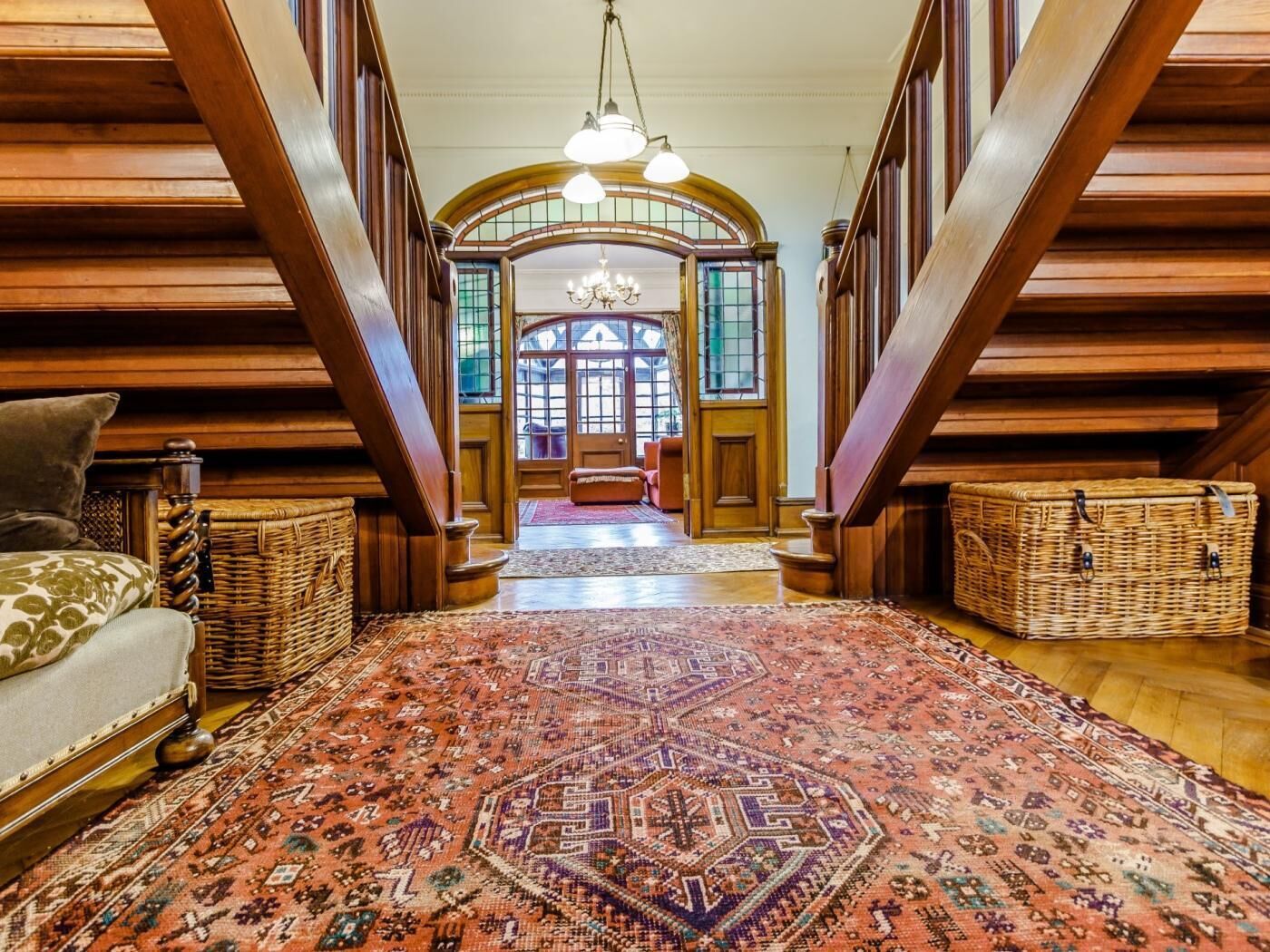 A grand hallway with a large, ornate rug, wooden paneling, and a chandelier.