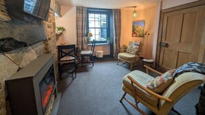 A cozy room with a stone wall, a fireplace, a window with curtains, and a wooden door. - 1 Bed in Lauder (oc-83459) (Lauder)