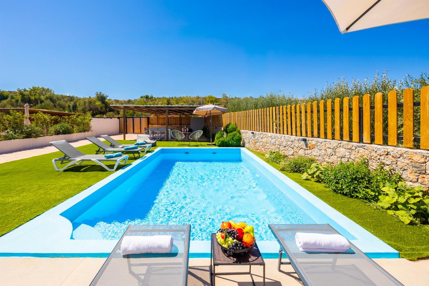 A swimming pool with lounge chairs and a table with fruit.